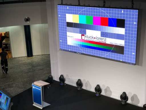 Bühne mit Podium, großem Bildschirm und Farbtestmustern im Hintergrund.